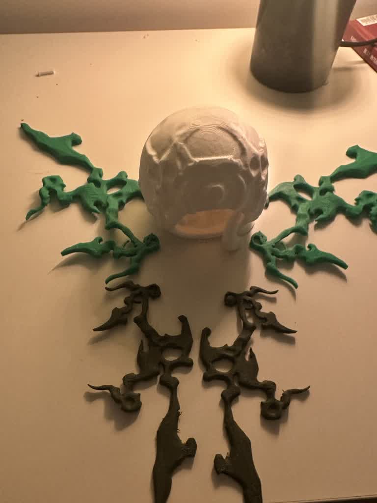 All 3D printed parts laid out: sphere body with eye textures, green and grey wing segments